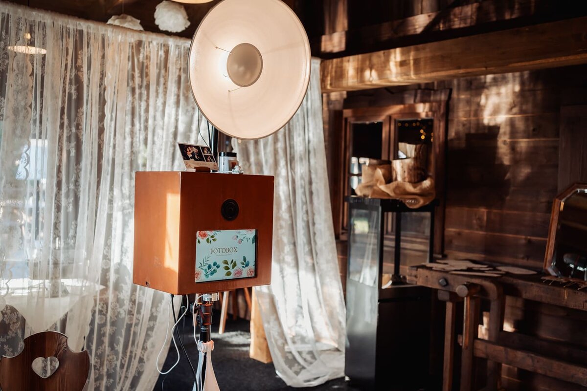 Die Fotobox mit Studioblitz in einer Scheune, dahinter Spitzenvorhänge